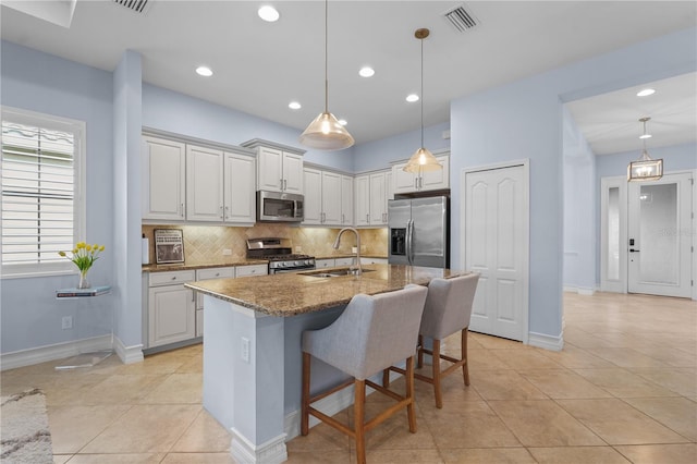 kitchen featuring a kitchen island with sink, hanging light fixtures, sink, dark stone countertops, and stainless steel appliances