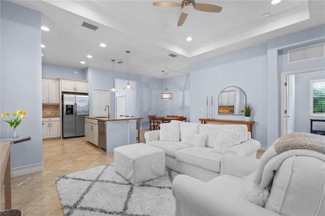 living room with light tile patterned floors, a tray ceiling, ceiling fan, and sink