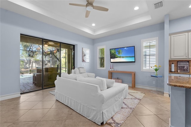 living room with ceiling fan, a raised ceiling, and light tile patterned floors