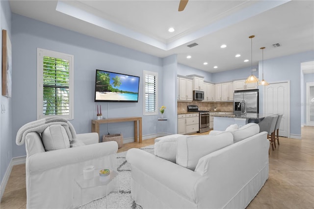 tiled living room featuring ceiling fan, sink, crown molding, and a tray ceiling