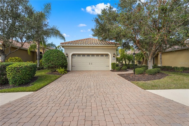 mediterranean / spanish-style home featuring a garage, decorative driveway, a tile roof, and stucco siding