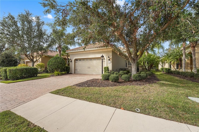 mediterranean / spanish-style home featuring decorative driveway, a tile roof, stucco siding, an attached garage, and a front yard