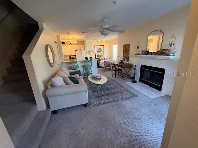 living room with carpet flooring, ceiling fan, and a tile fireplace