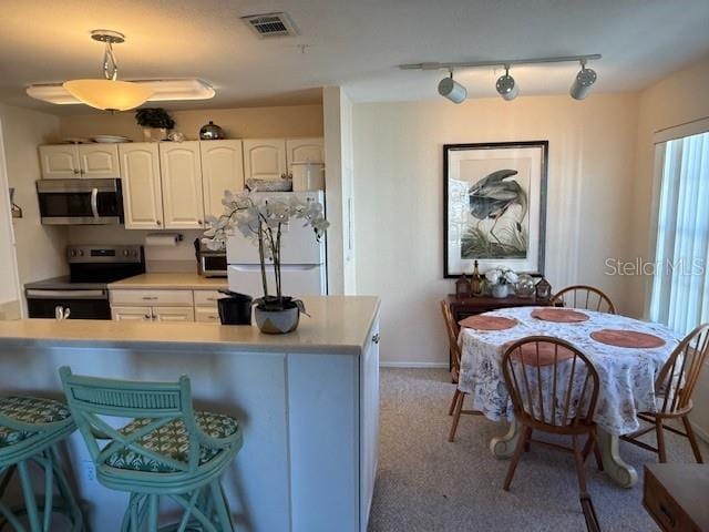 kitchen with white cabinetry, stainless steel appliances, pendant lighting, track lighting, and light carpet