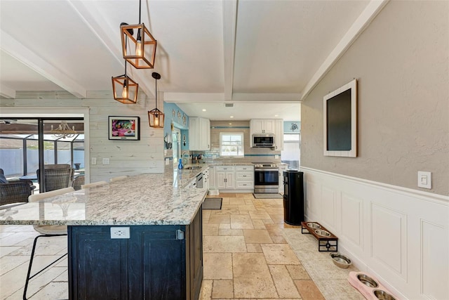 kitchen featuring pendant lighting, white cabinets, appliances with stainless steel finishes, beam ceiling, and a kitchen bar