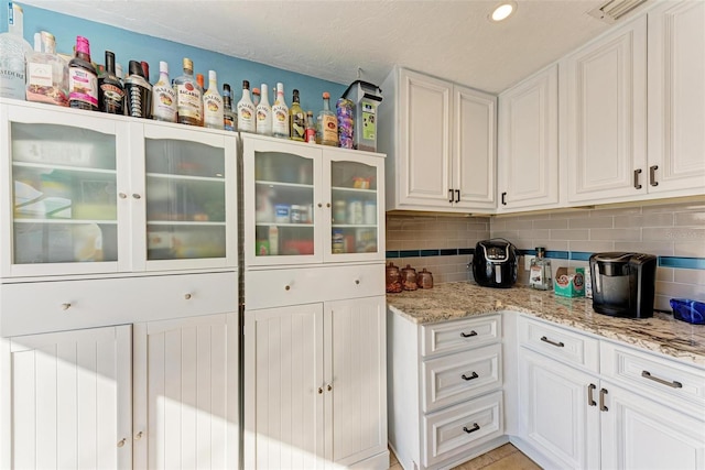 kitchen featuring white cabinetry, light stone countertops, and backsplash