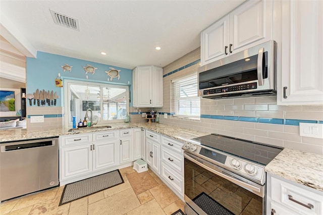 kitchen with appliances with stainless steel finishes, tasteful backsplash, light stone counters, sink, and white cabinetry