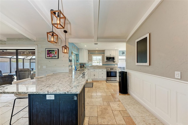 kitchen with stainless steel appliances, hanging light fixtures, white cabinets, beamed ceiling, and a kitchen breakfast bar