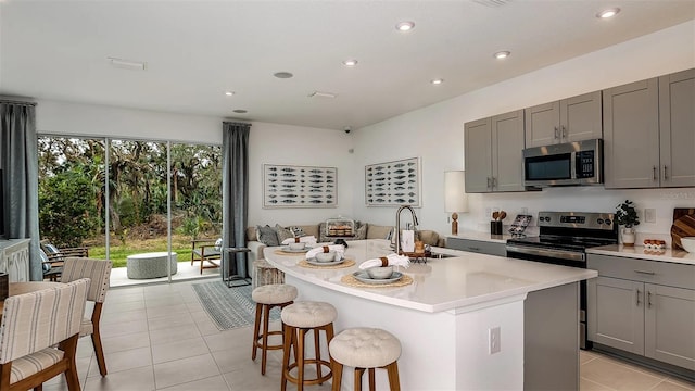 kitchen with gray cabinets, sink, stainless steel appliances, and a center island with sink