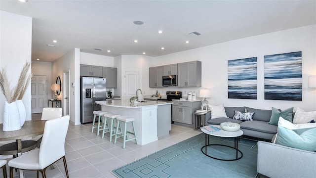 kitchen featuring gray cabinetry, sink, stainless steel appliances, an island with sink, and a breakfast bar area