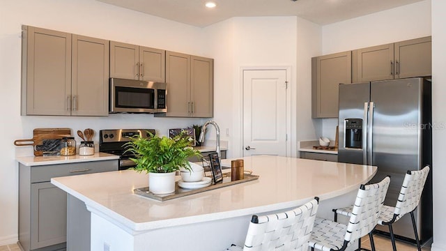 kitchen with a kitchen breakfast bar, gray cabinets, a center island with sink, and appliances with stainless steel finishes