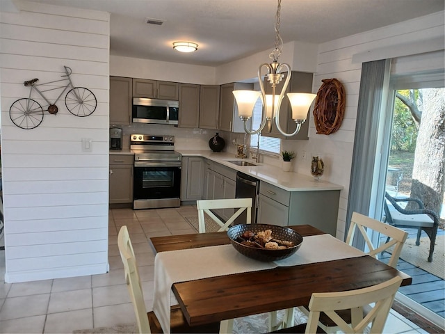 kitchen with gray cabinets, pendant lighting, stainless steel appliances, light tile patterned floors, and a chandelier