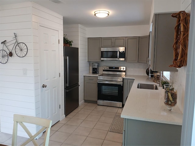 kitchen featuring light stone countertops, appliances with stainless steel finishes, sink, light tile patterned flooring, and gray cabinetry