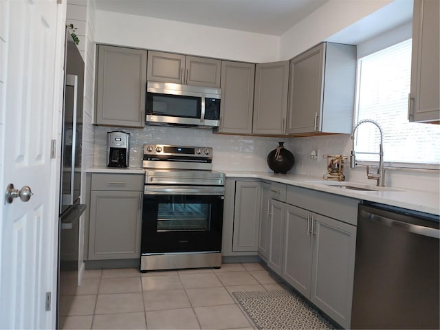 kitchen featuring light tile patterned floors, gray cabinets, appliances with stainless steel finishes, and sink