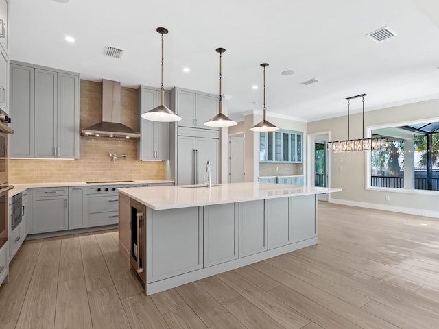 kitchen featuring a center island with sink, wall chimney exhaust hood, pendant lighting, and gray cabinetry