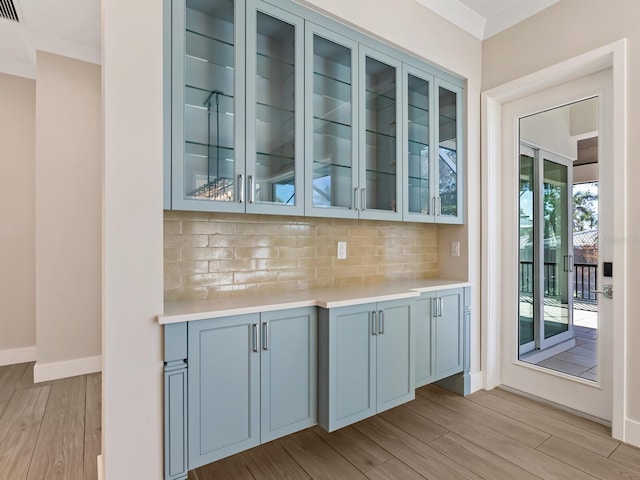 bar featuring backsplash, light hardwood / wood-style flooring, and ornamental molding