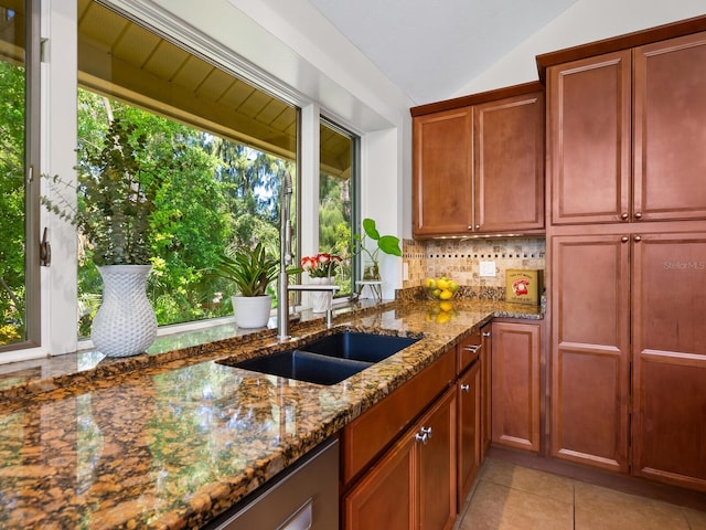 kitchen featuring light tile patterned floors, a sink, vaulted ceiling, tasteful backsplash, and dark stone countertops