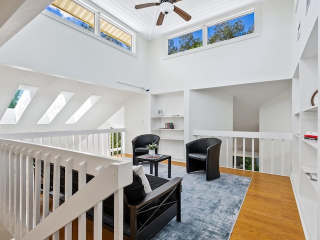 living room featuring hardwood / wood-style flooring, ceiling fan, a towering ceiling, and wooden ceiling