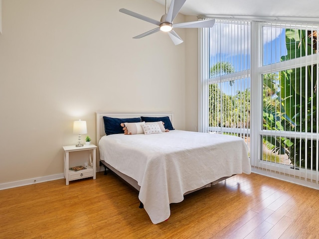 bedroom featuring a wall of windows, light wood-type flooring, a ceiling fan, and baseboards