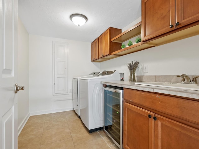 clothes washing area with cabinets, sink, wine cooler, separate washer and dryer, and light tile patterned flooring