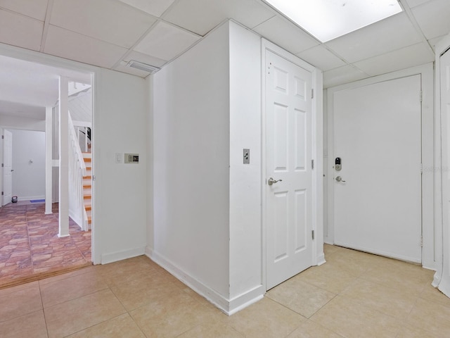 hall with a paneled ceiling, stairs, and baseboards