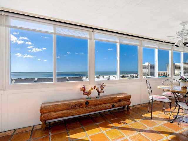 sunroom / solarium with ceiling fan, a water view, and a view of the beach