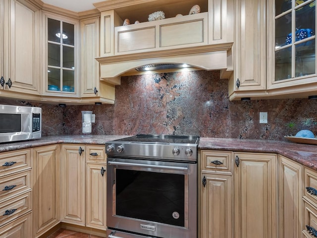 kitchen with backsplash, appliances with stainless steel finishes, dark stone counters, and tile patterned flooring