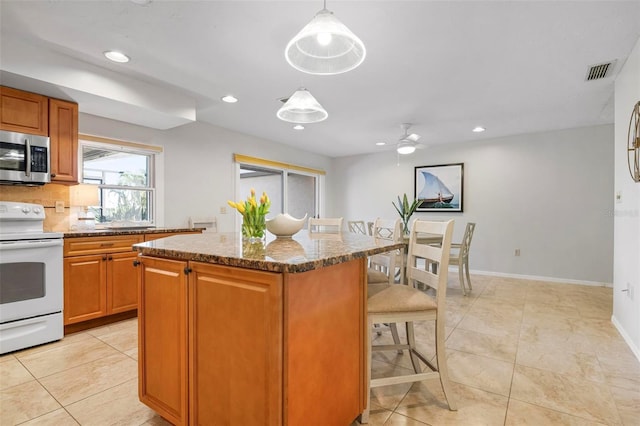 kitchen featuring a kitchen breakfast bar, white range with electric stovetop, ceiling fan, decorative light fixtures, and a kitchen island