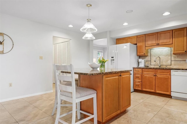 kitchen featuring sink, hanging light fixtures, dark stone counters, white appliances, and decorative backsplash