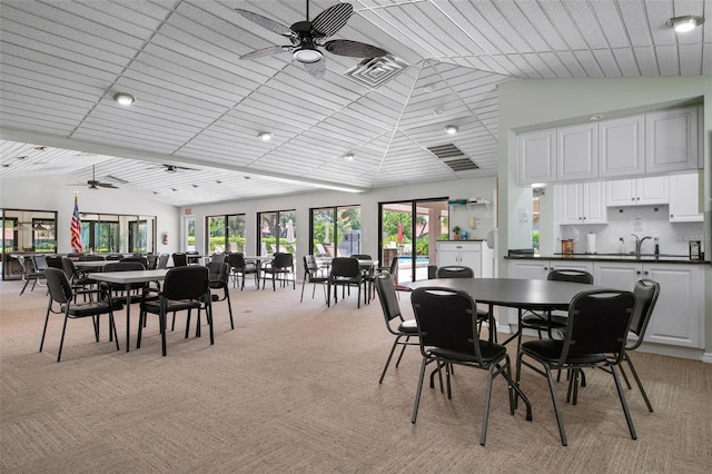 carpeted dining area featuring ceiling fan, lofted ceiling, and sink