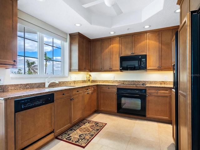 kitchen with black appliances, a raised ceiling, sink, ceiling fan, and light stone countertops