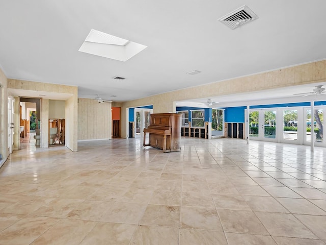 unfurnished living room with a skylight, wooden walls, french doors, and light tile patterned floors