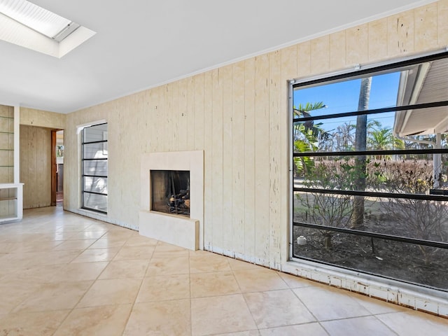 unfurnished living room with a skylight, wooden walls, and light tile patterned flooring