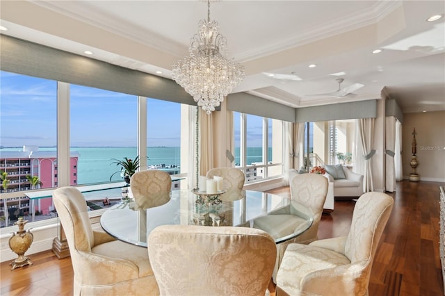 dining room featuring wood-type flooring, a water view, crown molding, and a notable chandelier