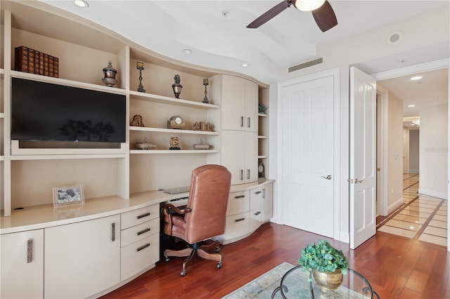 home office with ceiling fan, dark wood-type flooring, and built in desk