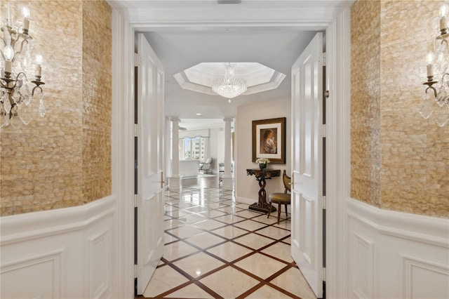 interior space featuring decorative columns, a tray ceiling, a chandelier, and ornamental molding