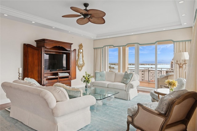 living room with light wood-type flooring, a raised ceiling, ceiling fan, and ornamental molding