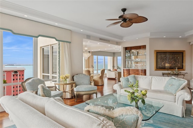 living room with ceiling fan with notable chandelier, hardwood / wood-style flooring, ornamental molding, and a water view