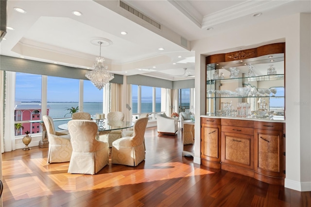 dining space with ornamental molding, a raised ceiling, wood-type flooring, a water view, and a chandelier