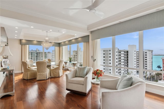 living room featuring ceiling fan with notable chandelier, a water view, crown molding, a tray ceiling, and dark hardwood / wood-style flooring