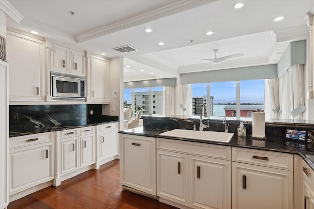 kitchen featuring ceiling fan, sink, dark stone countertops, white cabinets, and stainless steel microwave