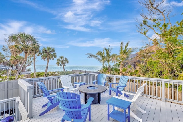 wooden terrace featuring a fire pit, a water view, and a view of the beach