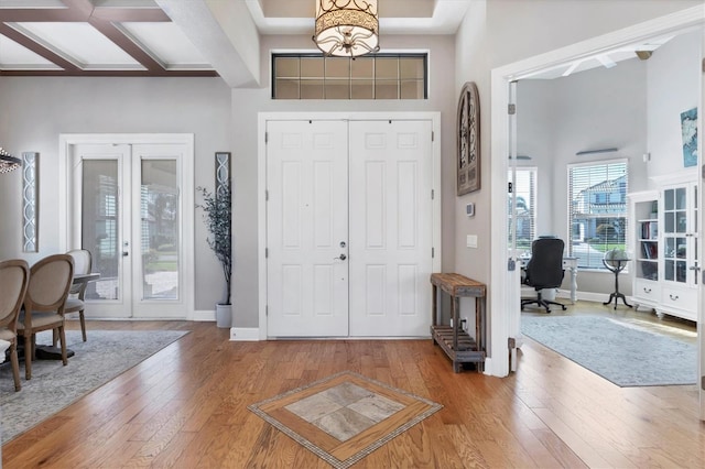 entrance foyer with hardwood / wood-style floors, an inviting chandelier, coffered ceiling, a towering ceiling, and beam ceiling