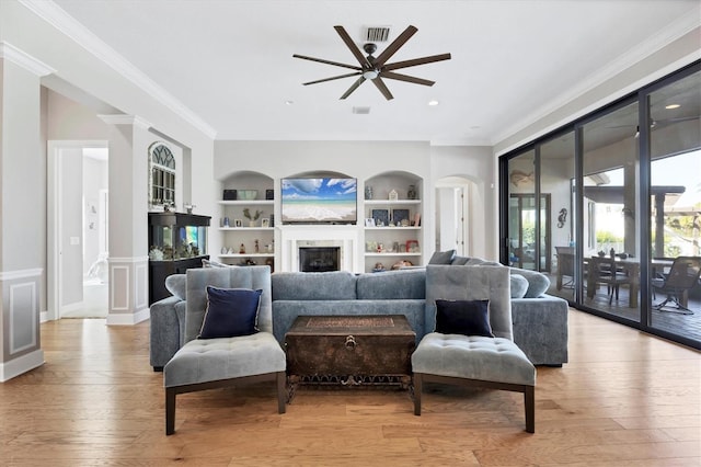 living room featuring built in shelves, ceiling fan, ornamental molding, and light hardwood / wood-style flooring