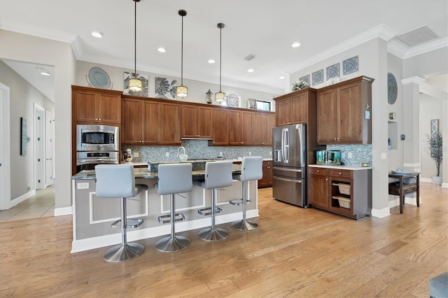 kitchen featuring hanging light fixtures, light wood-type flooring, a kitchen island with sink, and appliances with stainless steel finishes