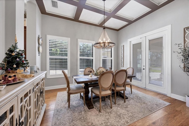 dining area with french doors, light wood-type flooring, coffered ceiling, beam ceiling, and a notable chandelier