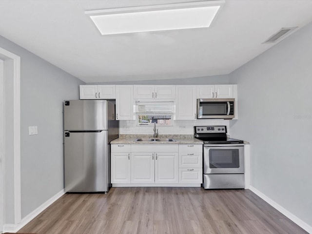 kitchen featuring sink, light hardwood / wood-style floors, lofted ceiling, white cabinets, and appliances with stainless steel finishes