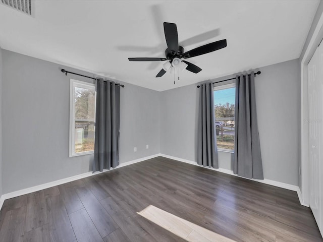 empty room featuring ceiling fan, dark wood-type flooring, and a healthy amount of sunlight