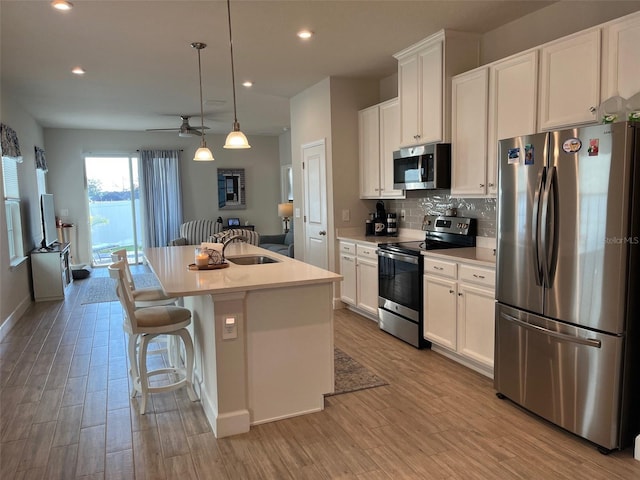 kitchen with white cabinetry, hanging light fixtures, a kitchen island with sink, a breakfast bar, and appliances with stainless steel finishes