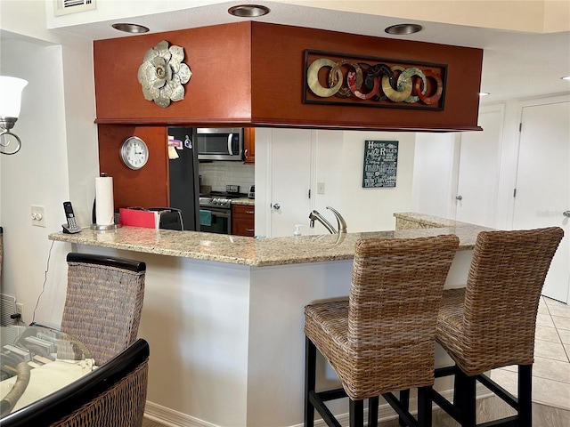 4445 46th Ave W, Bradenton, FL 34210 - kitchen featuring appliances with stainless steel finishes, backsplash, a peninsula, light stone countertops, and a kitchen bar